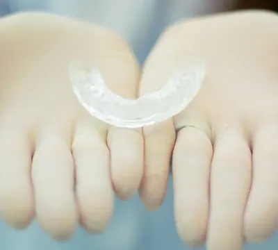 Gutieră dentară transparentă ținută în mâini cu mănuși.