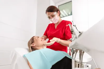 Medic dentist alături de o pacientă zâmbind în scaunul dentar.