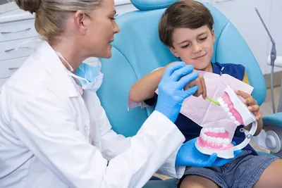 Copil care învață periajul pe un model dentar, alături de medic.